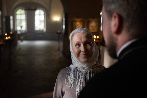A senior woman and a priest sharing a warm moment in a church interior, with ambient candlelight.