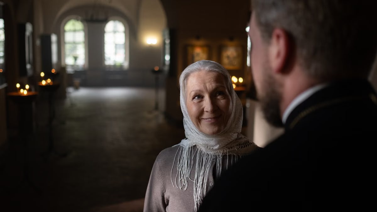 A senior woman and a priest sharing a warm moment in a church interior, with ambient candlelight.
