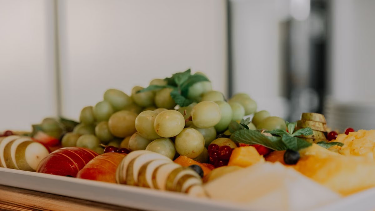 A vibrant assortment of fruits including grapes, apples, and berries on a white tray.